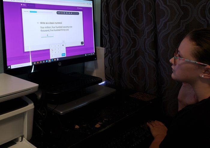 girl wearing glasses looking at computer screen while using mouse to click answer in online math curriculum