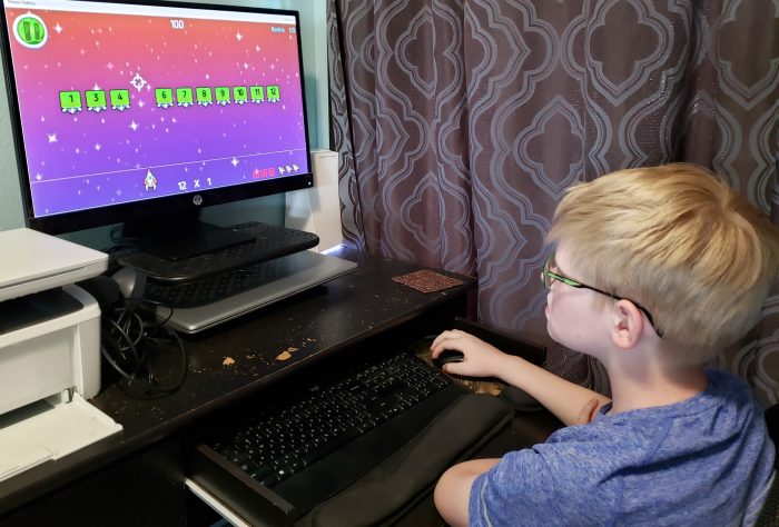 boy wearing glasses playing multiplication practice game with his online math curriculum on computer