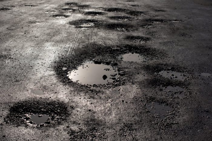 potholes in asphalt of a road with puddles in them from recent rain
