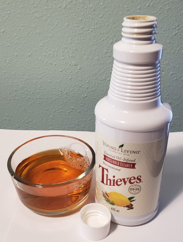 glass bowl holding amber colored fluid of young living thieves household cleaner next to product bottle and cap