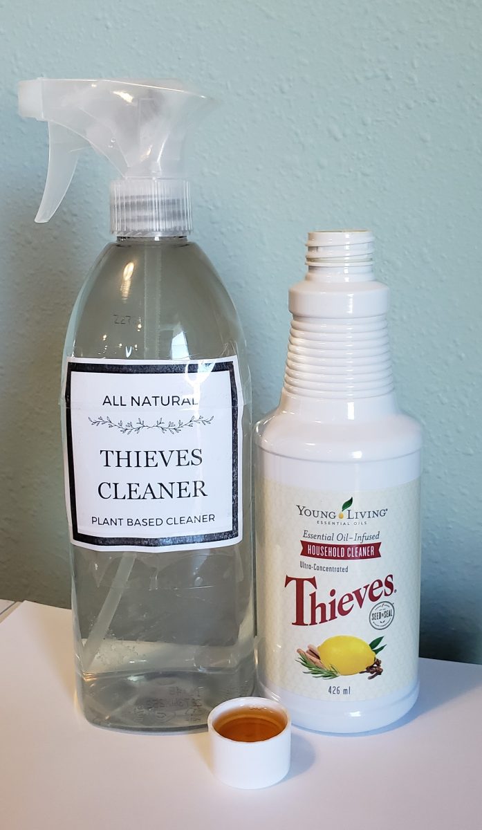 plastic spray bottle of all natural thieves cleaner plant based cleaner mixed with water minimalistic label on it next to young living thieves household cleaner bottle and capful of liquid