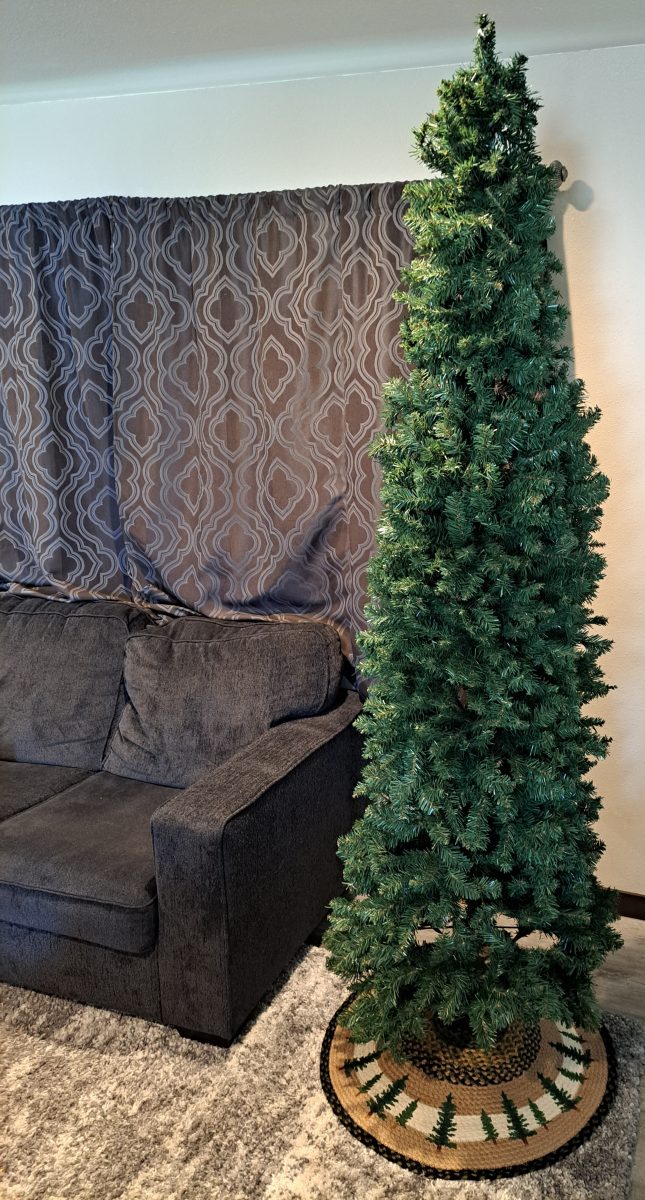 artificial tree with a printed jute christmas tree skirt that has a tall tree design printed on the skirt next to a living room couch