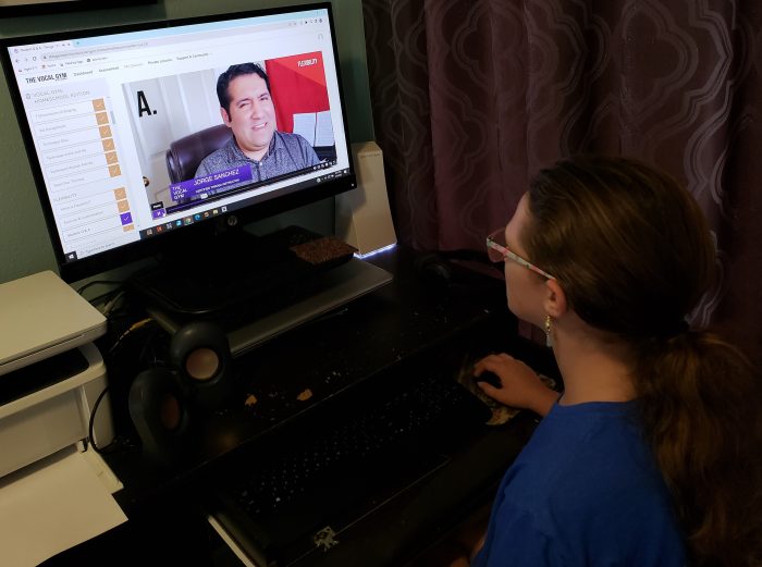 girl with hand on computer mouse watches a teacher online on large monitor teaching her singing lessons and flexibility