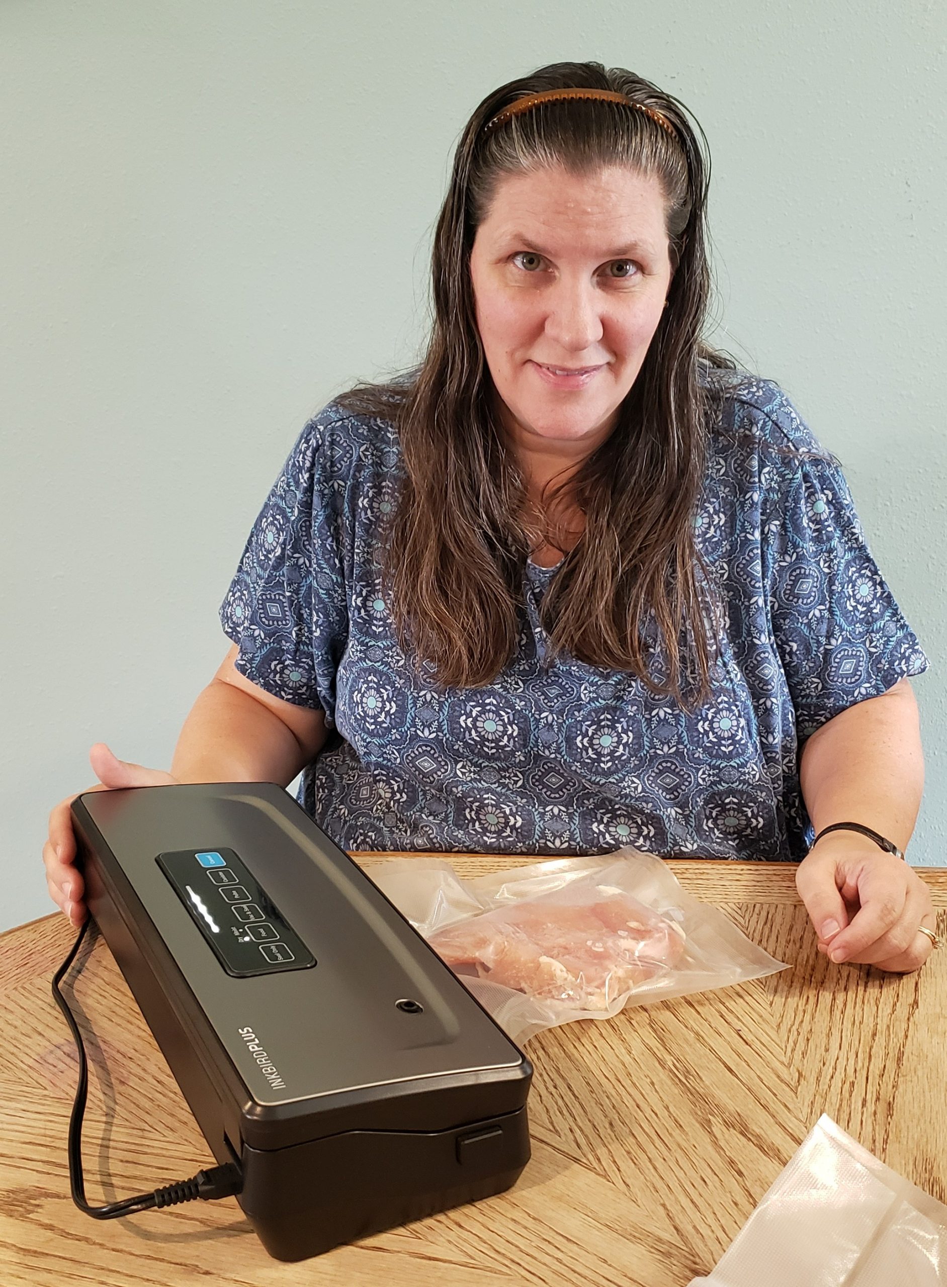 woman with inkbird plus vacuum sealer while it is sealing a chicken breast in a bag