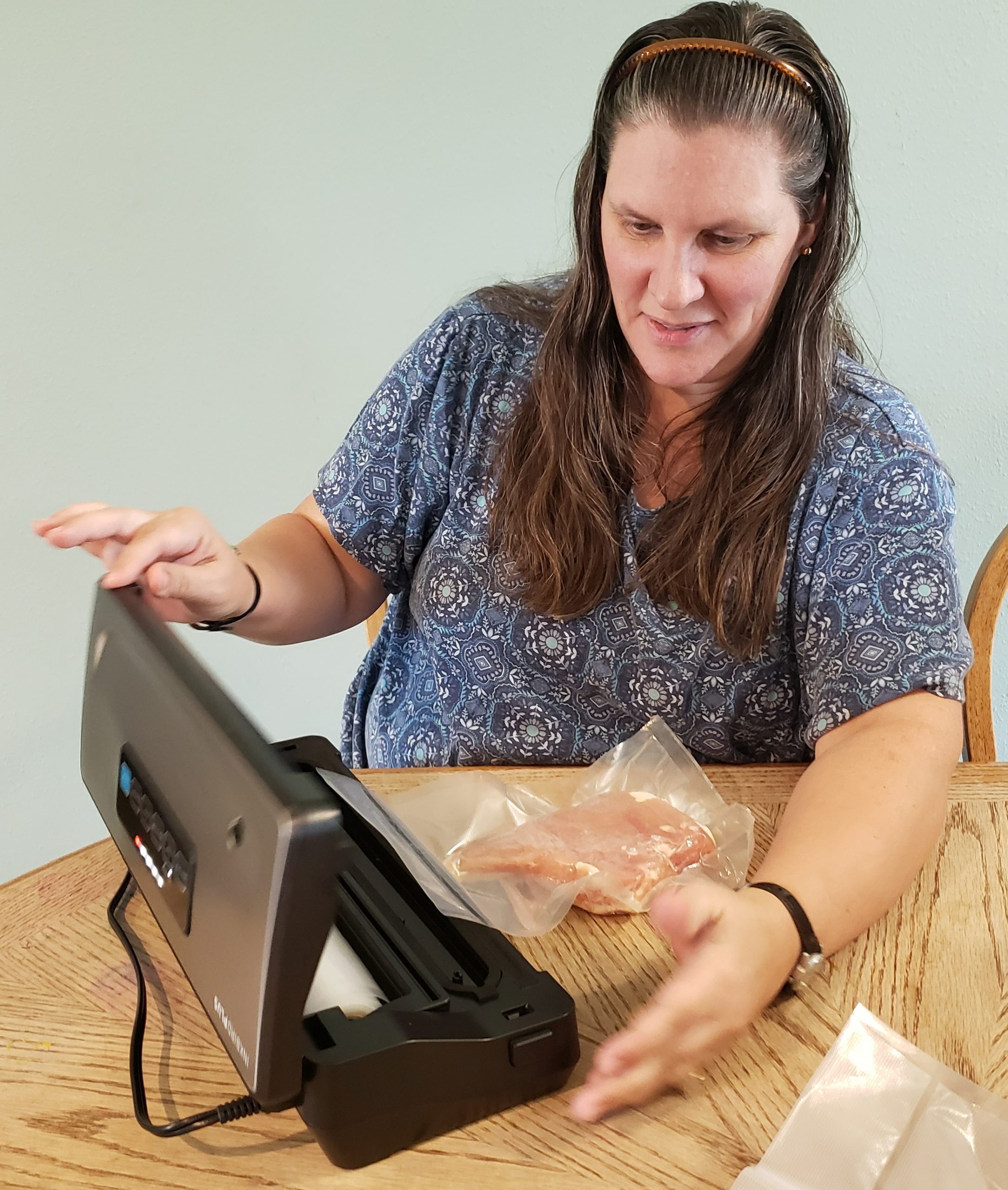 woman opening the inkbird plus vacuum sealer after it has vacuum sealed a chicken breast