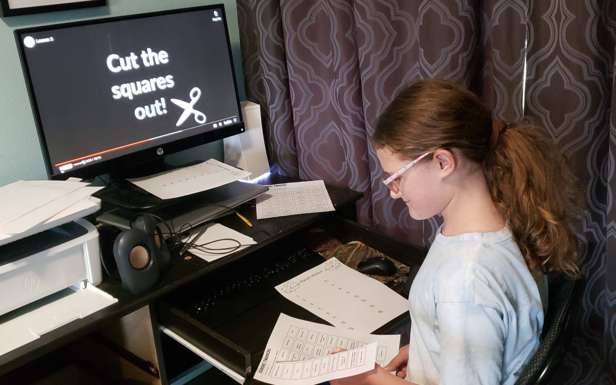girl sitting at desk cutting word squares out of paper for an activity computer monitor says cut the squares out