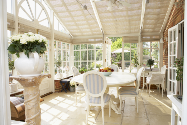 conservatory sun room addition of a home with white dining table chairs vase of white flowers on stand