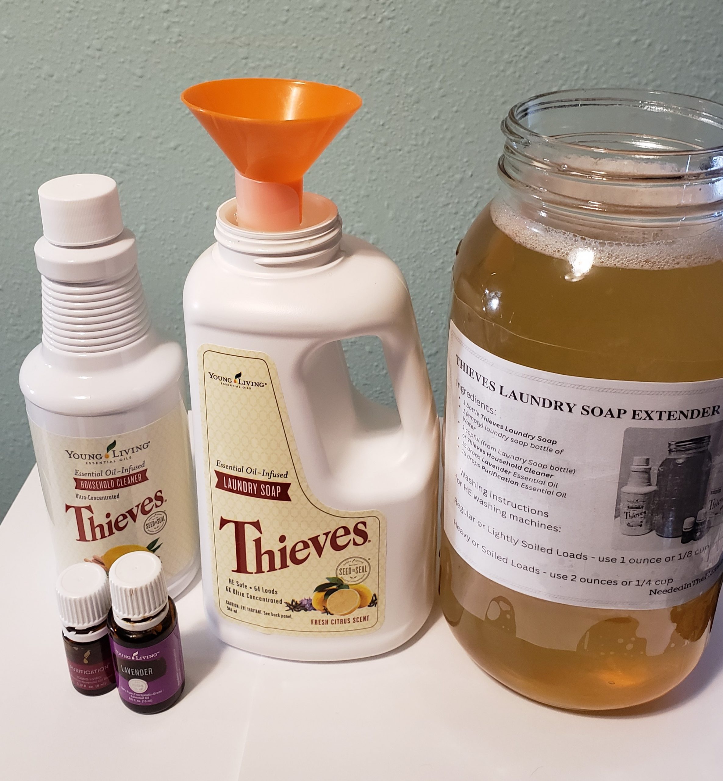 young living thieves household cleaner  and laundry soap with orange funnel next to glass jar filled with amber fluid and recipe taped to front purification blend and lavender essential oil