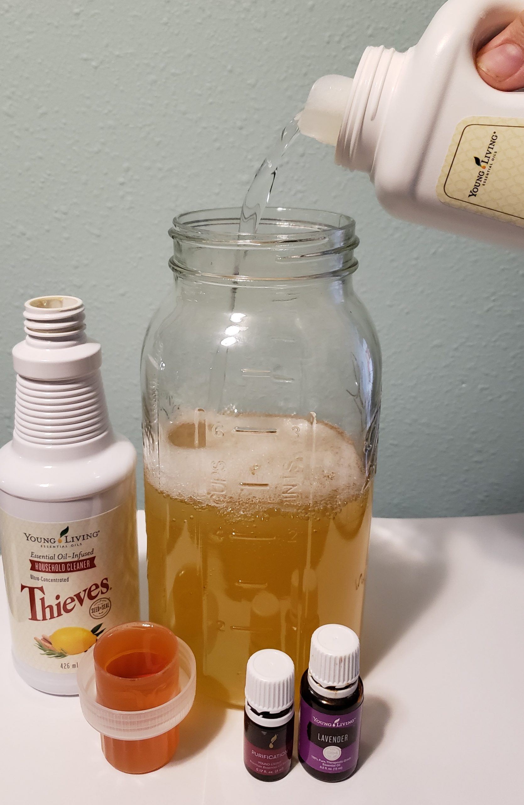water being poured into large glass jar next to young living thieves household cleaner and purification blend and lavender essential oil