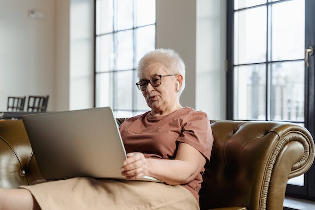 retired woman learning on a laptop sitting on a couch about retirement benefits she can get