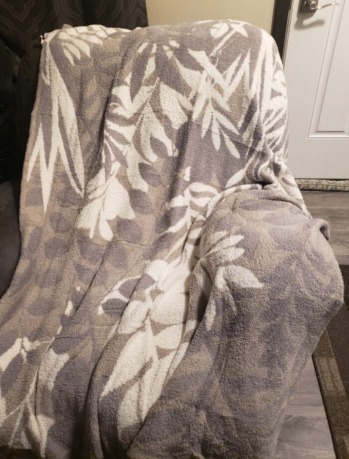 snuggle throw blanket with tropical leaf design in tan white gray color draped over a rocking chair in a living room