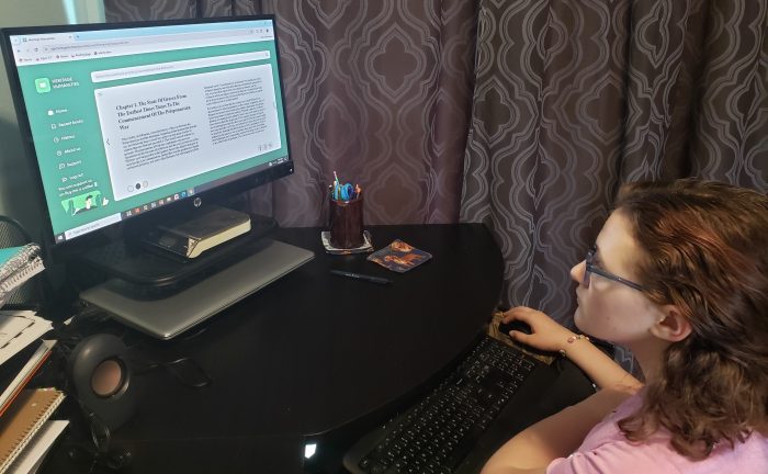 teen girl wearing glasses and looking at computer screen with white background page and black letters reading a book online