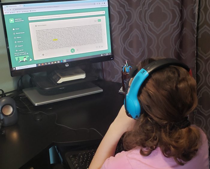 teen girl with headphones on looking at screen with a beige page of black words with one word highlighted in yellow