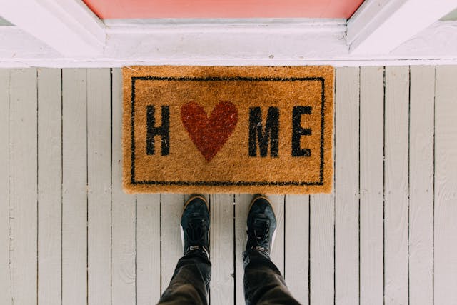 persons feet near door mat that says home with heart as the o