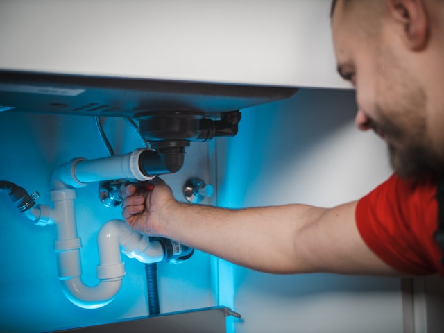 man checking pvc plumbing pipes under sink