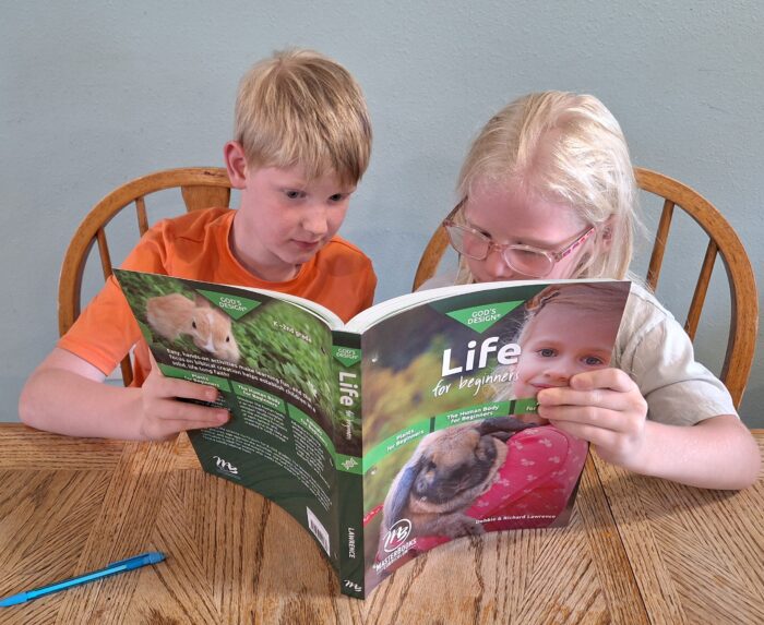 boy and girl holding elementary science curriculum book up as they look at it more closely