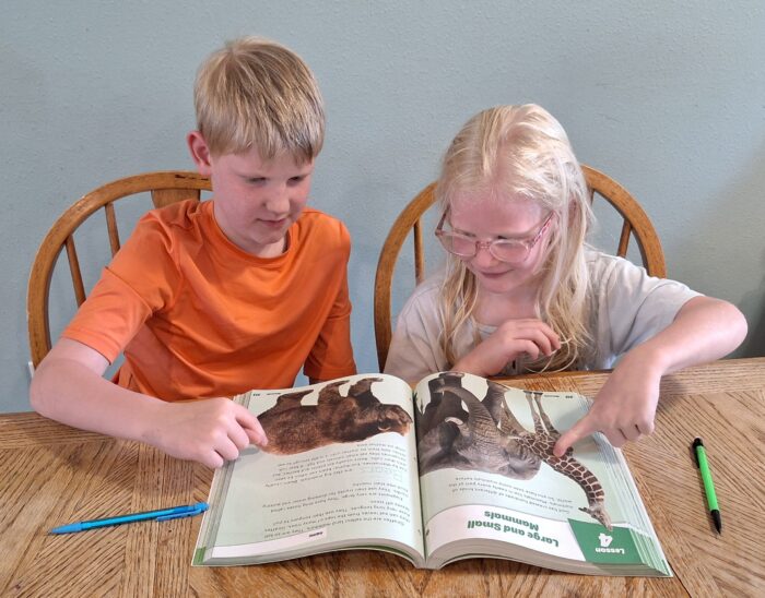 boy and girl pointing to animal pictures in their homeschool science curriculum workbook
