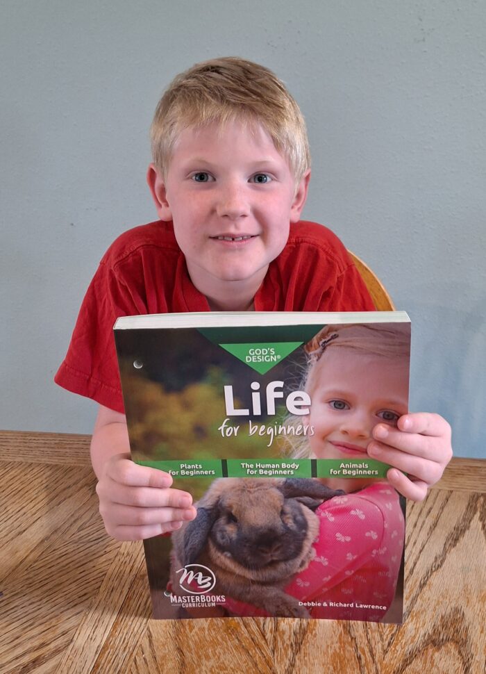 boy holding homeschool science workbook gods design life for beginners 