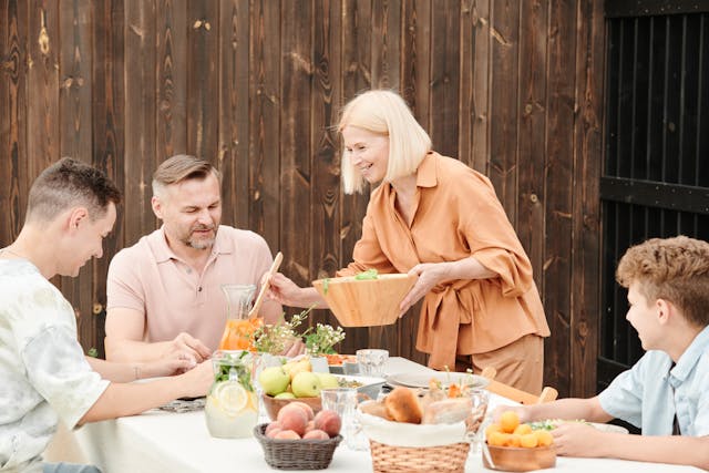 family eating outside with woman serving a man salad