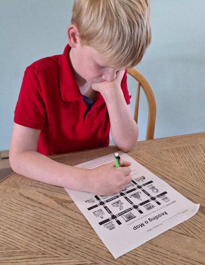 boy looking down at his map reading worksheet for homeschool as he writes on it