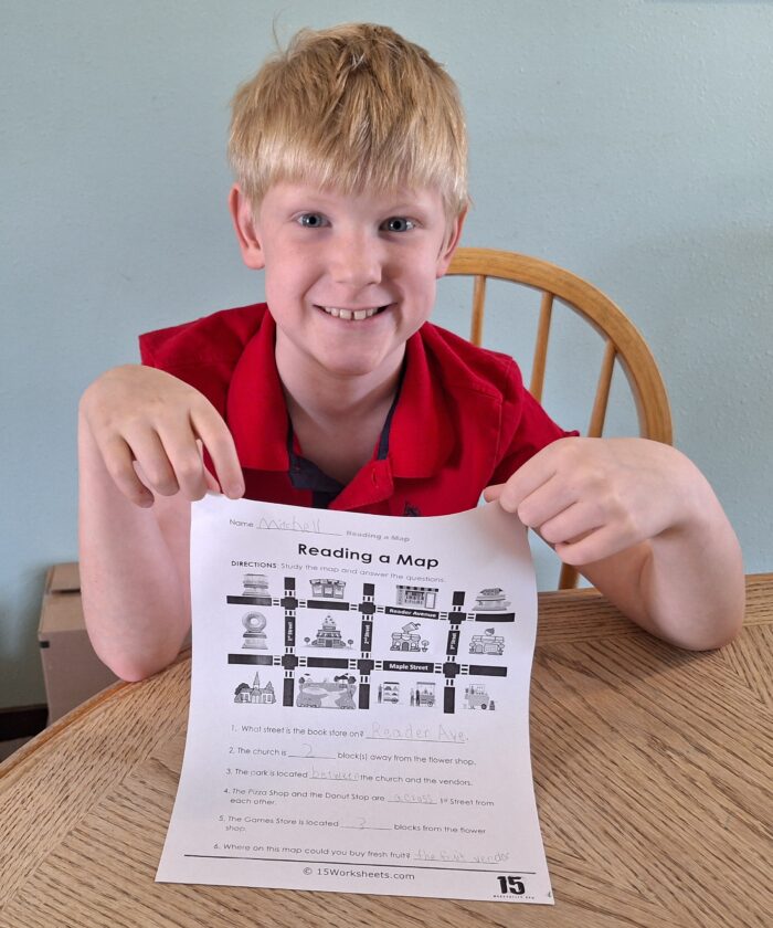 smiling boy holding his geography reading a map worksheet for homeschool