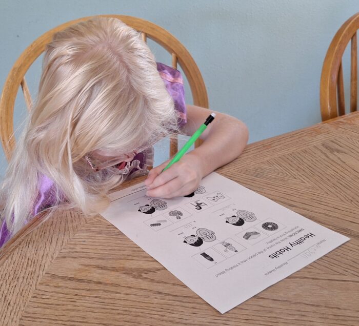 girl looking down as she writes on her school worksheet for health