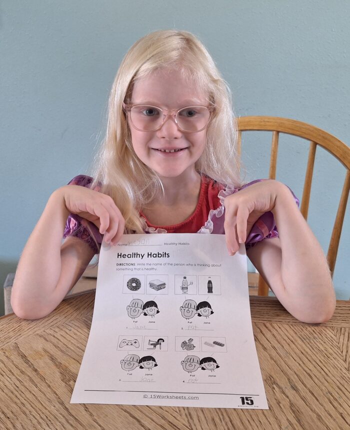 girl wearing glasses holding up her completed health worksheet