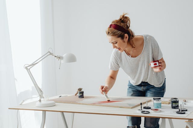 woman painting a wooden board with disgusted look on her face