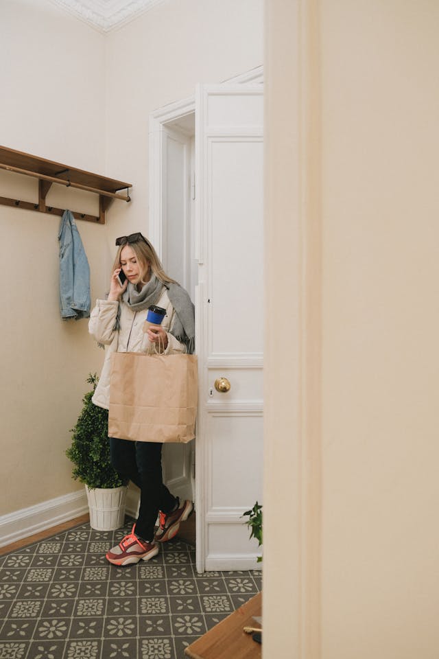 woman on phone in front hallway with shoppping bag and coffee while talking on the phone
