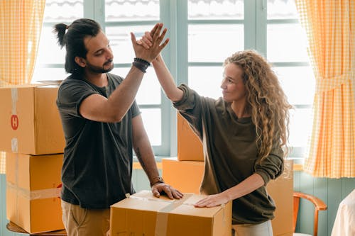 man and woman touching hands in air after taping up the last box when moving