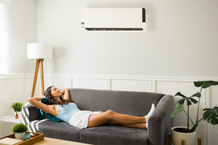 The quiet system shaping how your home feels everyday, your HVAC, influences energy levels, allergies, focus, and even mood on a daily basis. woman laying comfortably on her couch under her air conditioning unit on a hot day