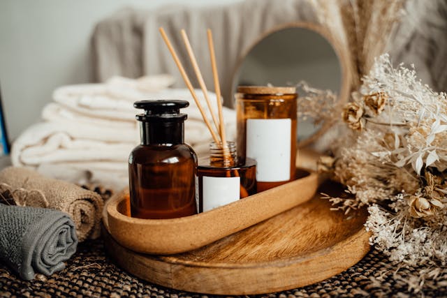 a setting of bath washcloths glass containers and sticks in a vanilla essence liquid with bath towels and mirror in background