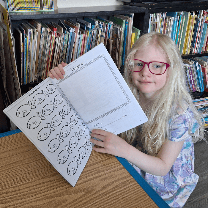 girl wearing glasses holding a workbook with pictures of fish and I caught it blank square area