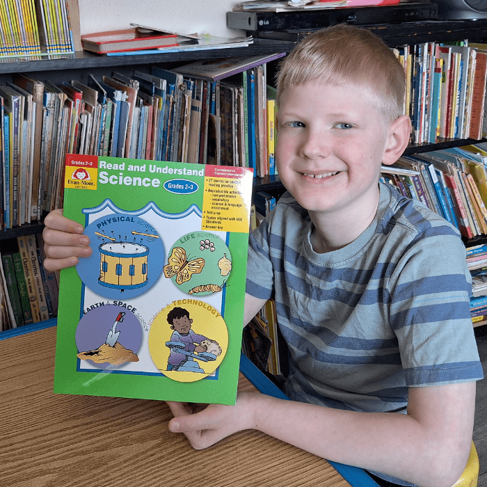 smiling boy holding evan moor read and understand science workbook for grade 2 grade 3