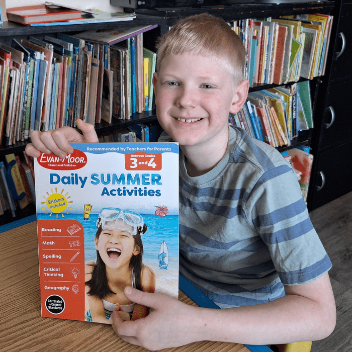 smiling boy holding evan moor daily summer activities workbook grade 3 and grade 4