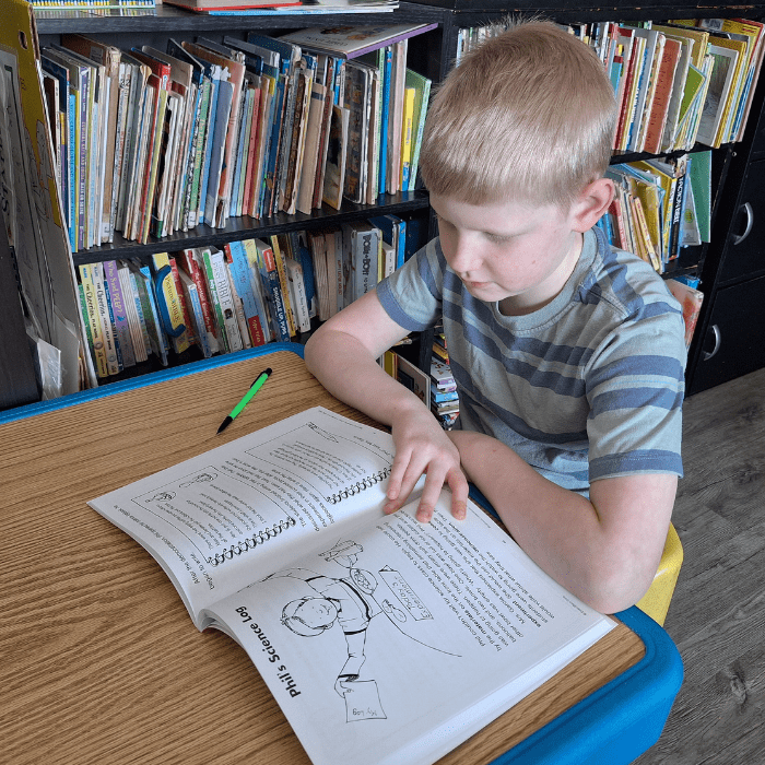 boy sitting at a small table looking at his workbook opened to page about phils science log