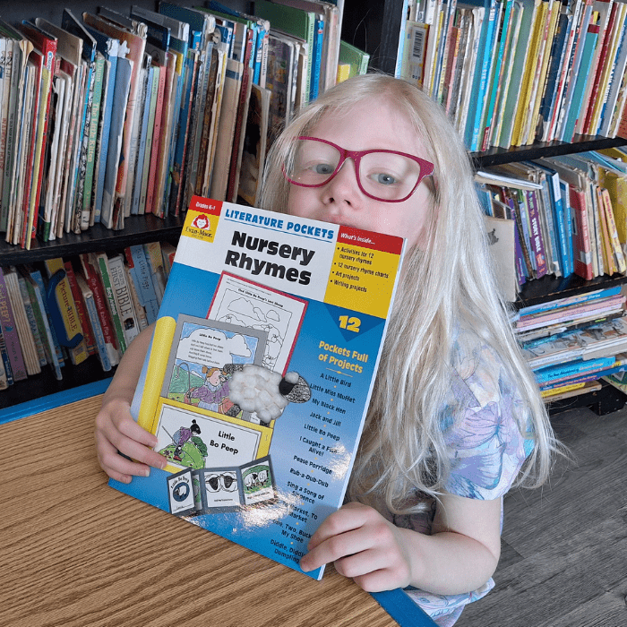 girl holding educational workbook called literature pockets nursery rhymes for grade k grade 1