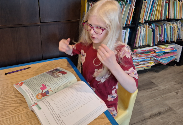 girl wearing glasses talking with her hands moving while using a math workbook