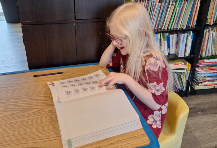smiling girl looking at a cutout page in her math workbook from master books