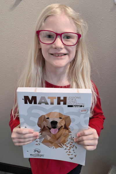 smiling girl in glasses holding her math workbook from master books
