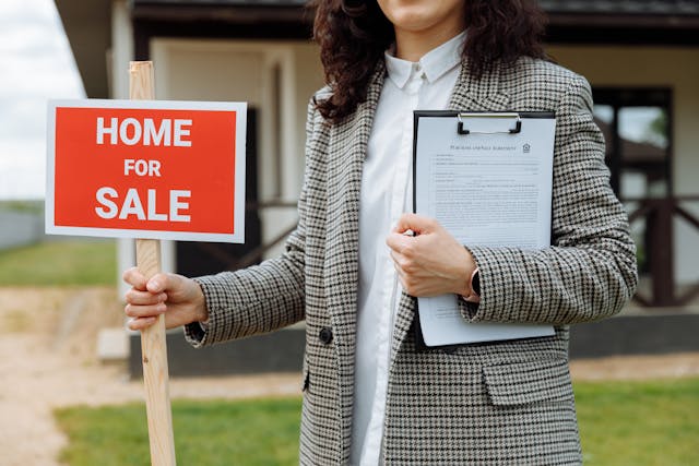 Comparing real estate agents is pivotal before selling your home. Choose right and your experience will be less stressful and less expensive. woman holding home for sale sign and a clipboard