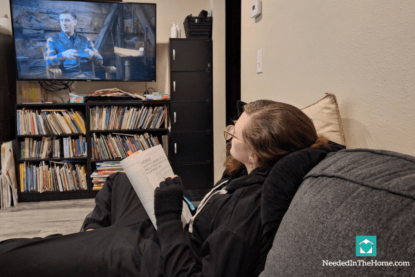 teen girl watching a man speak on a video on tv monitor while holding steadfast notebook