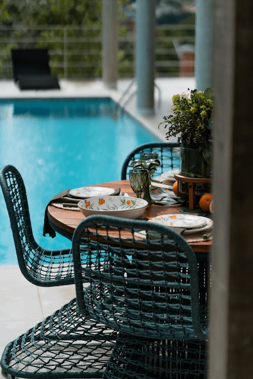 table setting next to a backyard swimming pool with wicker outdoor chairs