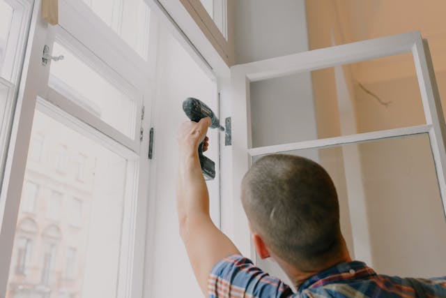 man using a drill on hinge hardware of an open window