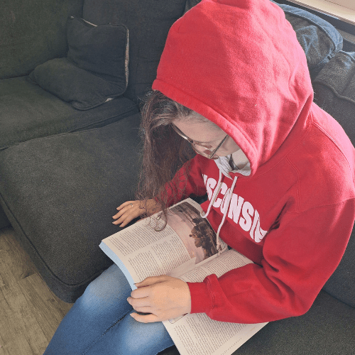 teen girl in red hoodie reading her american history book while sitting on the couch