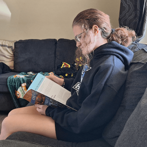teen girl with ponytail in hair reading her history textbook while sitting on the couch