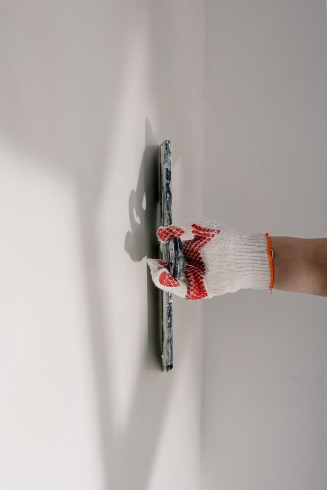 gloved hand smoothing out a panel of drywall