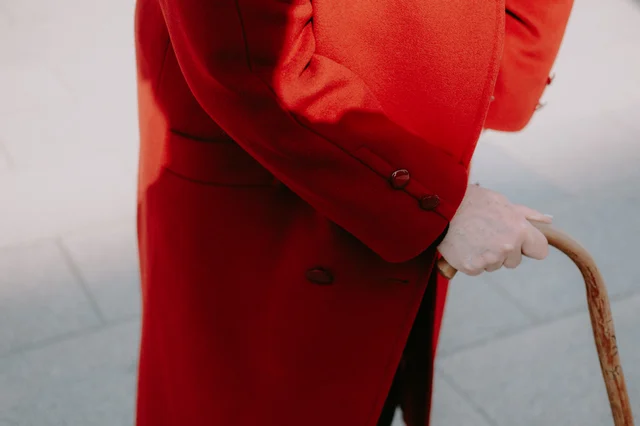 elderly person in red coat walking with wooden cane