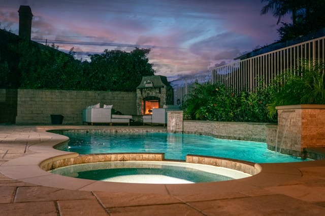 custom swimming pool in backyard at night near outdoor couch and fireplace