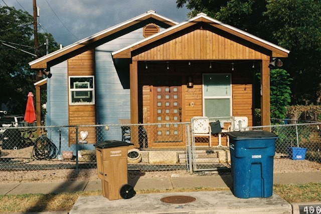 From the water swirling down your drains to all that packaging from online shopping, our household waste has a big impact on the environment. small house with fence around it and trash bins in front
